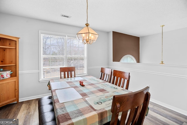 dining room with visible vents, a textured ceiling, wood finished floors, a chandelier, and baseboards