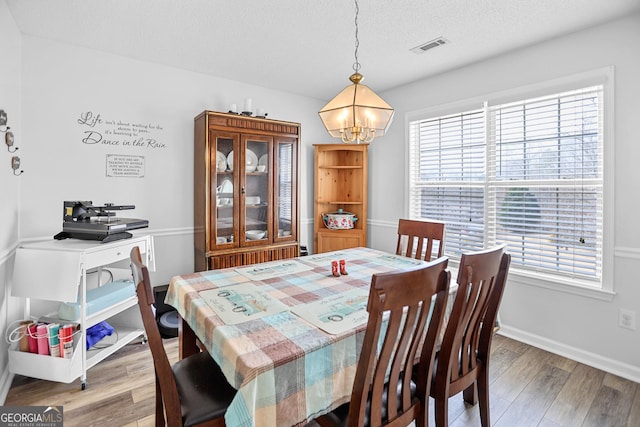 dining area with baseboards, visible vents, a textured ceiling, light wood-type flooring, and a notable chandelier