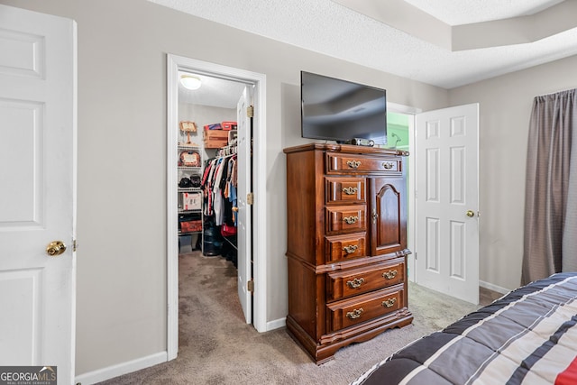 bedroom with a textured ceiling, light colored carpet, baseboards, a closet, and a walk in closet