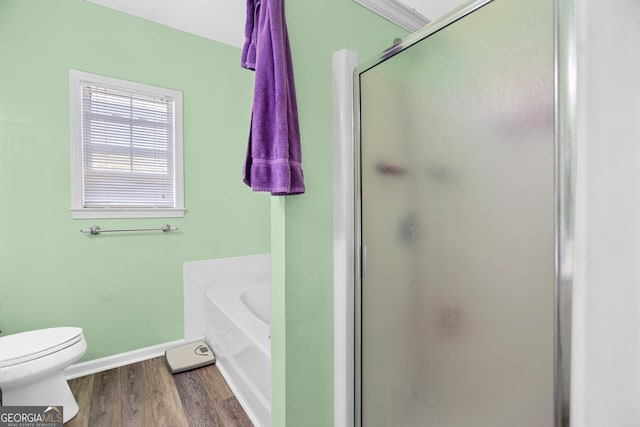 bathroom with a garden tub, toilet, a stall shower, wood finished floors, and baseboards