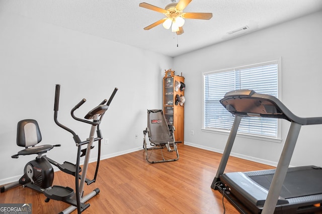 exercise area with light wood-type flooring, baseboards, visible vents, and a textured ceiling