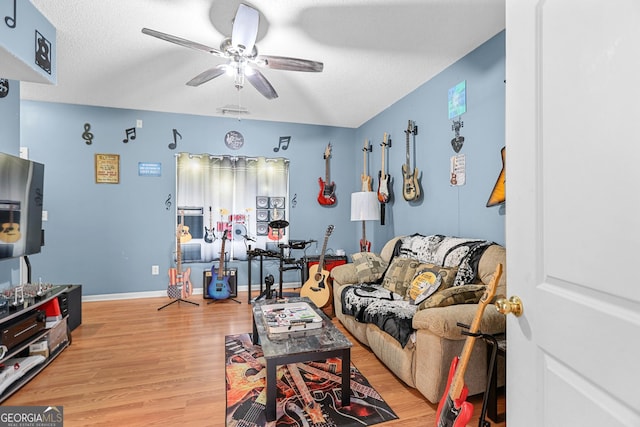 living area featuring a textured ceiling, light wood-type flooring, a ceiling fan, and baseboards