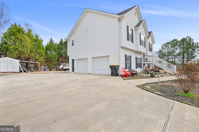 view of side of property with concrete driveway, a shed, a garage, an outdoor structure, and stairs