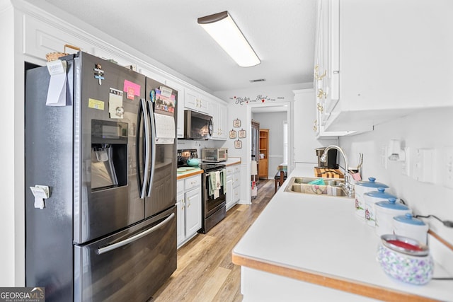 kitchen with light wood finished floors, white cabinets, stainless steel appliances, light countertops, and a sink