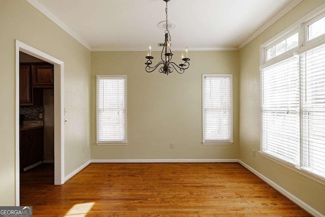 unfurnished dining area featuring a notable chandelier, ornamental molding, light wood-type flooring, and baseboards