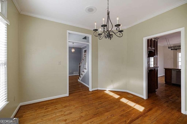 unfurnished dining area featuring baseboards, stairway, wood finished floors, crown molding, and a notable chandelier