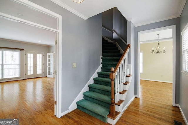 stairway featuring french doors, baseboards, an inviting chandelier, wood finished floors, and crown molding