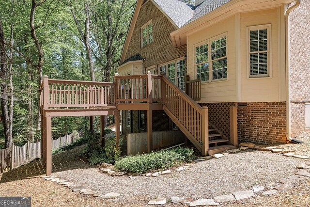 exterior space featuring stairway, a deck, fence, brick siding, and roof with shingles