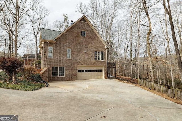 view of home's exterior featuring driveway, brick siding, an attached garage, and fence