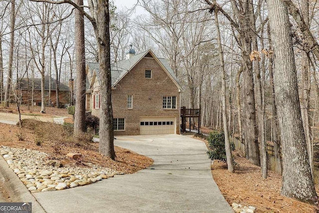 view of home's exterior featuring driveway, brick siding, a chimney, and an attached garage