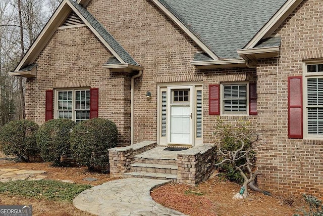 entrance to property featuring a shingled roof and brick siding