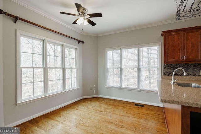 unfurnished dining area with a sink, visible vents, baseboards, light wood-style floors, and ornamental molding