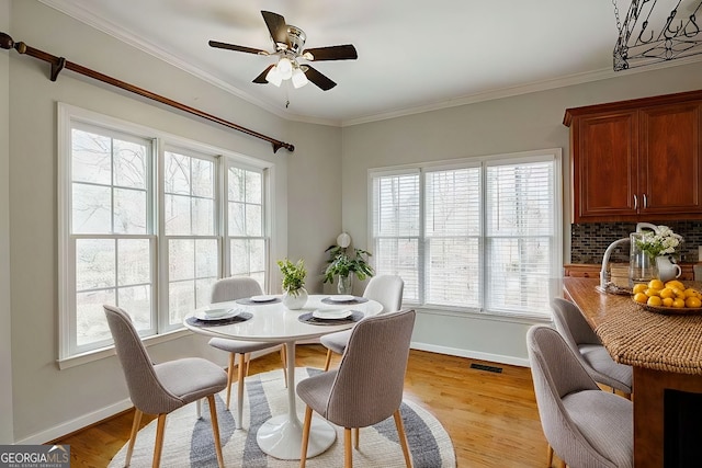 dining room featuring wood finished floors, visible vents, crown molding, baseboards, and ceiling fan