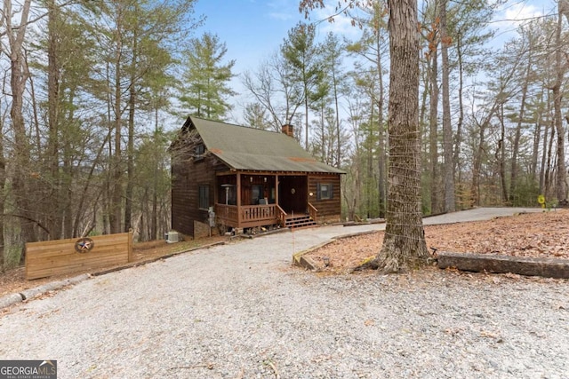 rustic home with gravel driveway, covered porch, and a chimney