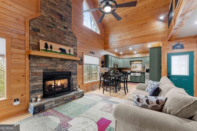 living room with light wood-style floors, high vaulted ceiling, ceiling fan, and wooden walls