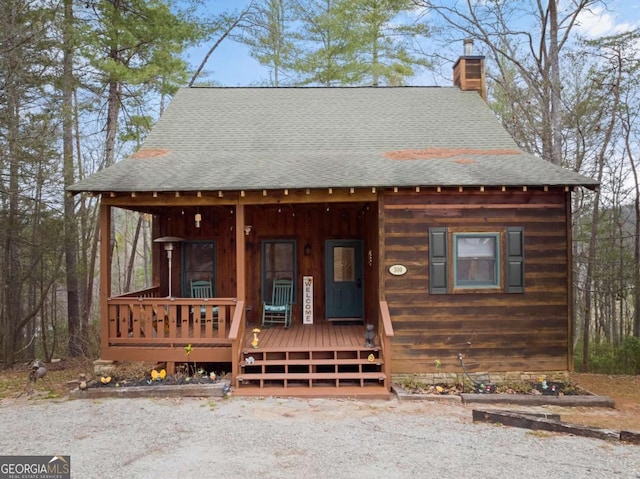 chalet / cabin featuring covered porch, roof with shingles, and a chimney