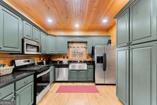 kitchen featuring appliances with stainless steel finishes, dark countertops, a sink, and green cabinets