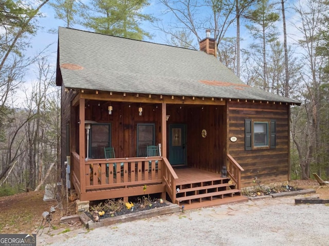 chalet / cabin featuring covered porch, a shingled roof, and a chimney