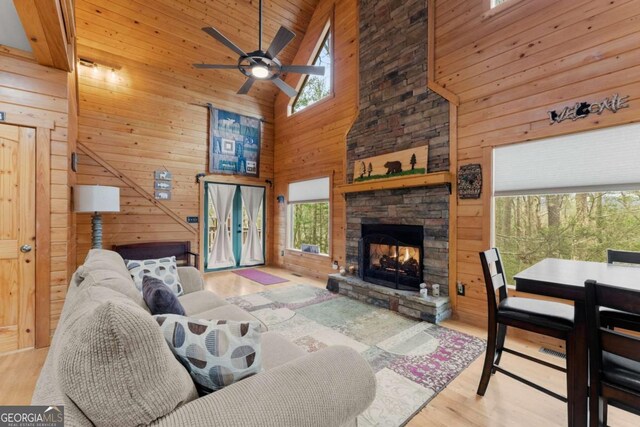 living area with wooden walls, wooden ceiling, wood finished floors, a stone fireplace, and high vaulted ceiling