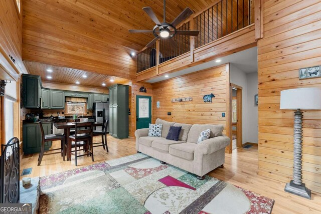 living room with a stone fireplace, wood walls, a ceiling fan, and light wood-style floors