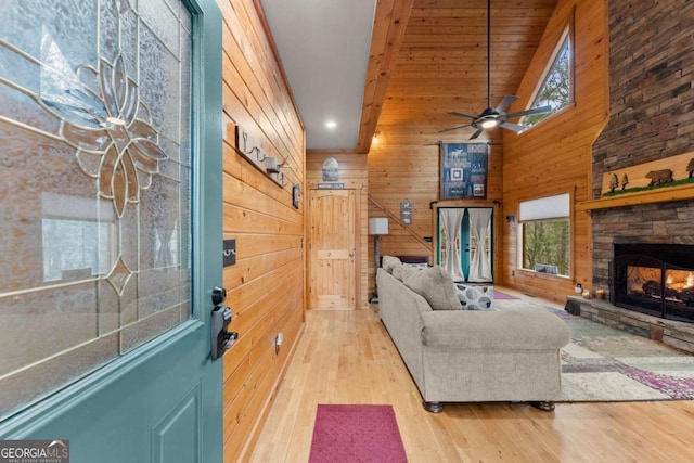 living area with wood finished floors, a stone fireplace, wooden walls, recessed lighting, and a ceiling fan