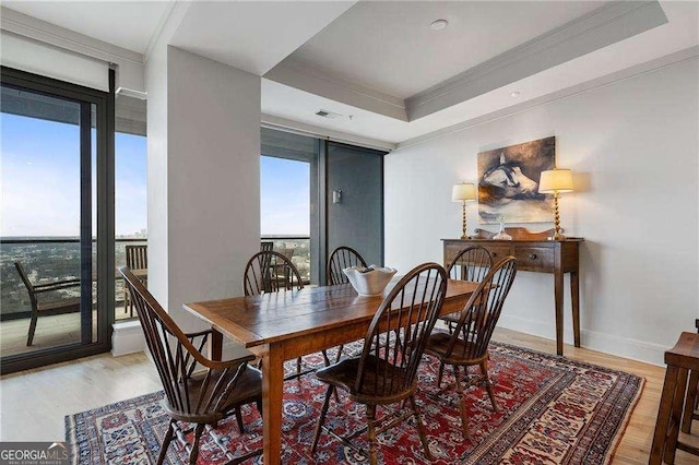 dining area with light wood-style floors, baseboards, a tray ceiling, and ornamental molding