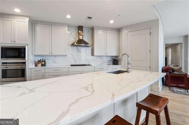 kitchen featuring a sink, black appliances, light stone countertops, wall chimney exhaust hood, and tasteful backsplash