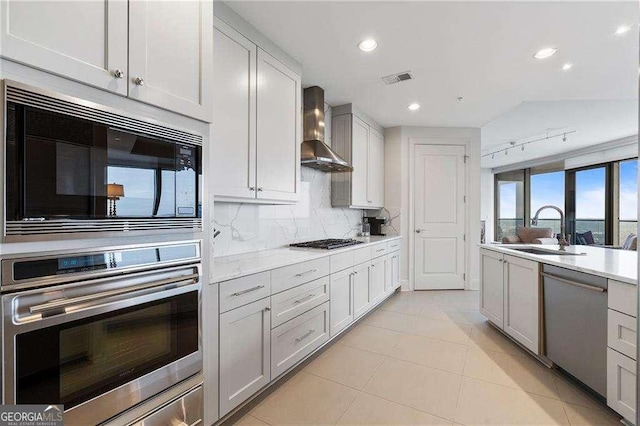 kitchen with stainless steel appliances, a sink, light countertops, wall chimney range hood, and decorative backsplash