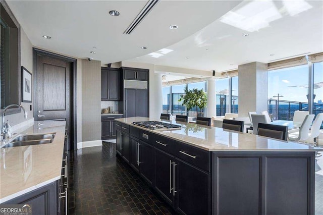 kitchen with light stone counters, stainless steel gas cooktop, a sink, a large island, and tasteful backsplash