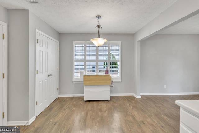 unfurnished dining area with baseboards, a textured ceiling, and wood finished floors