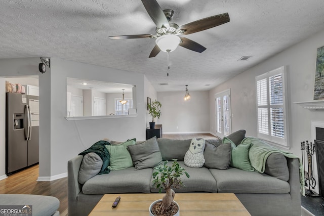 living room with visible vents, a textured ceiling, wood finished floors, a fireplace, and baseboards