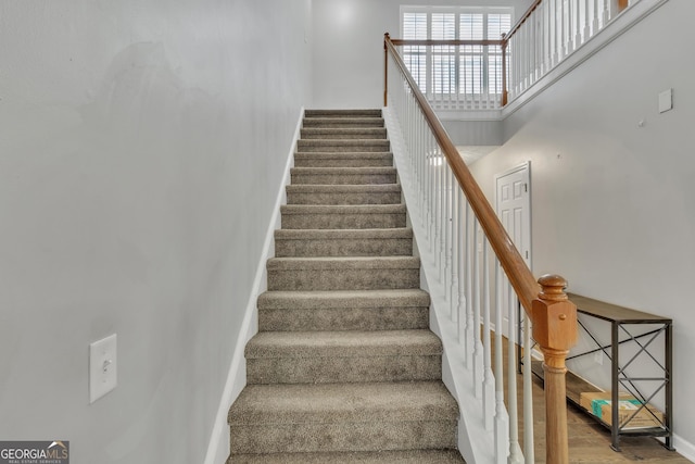 stairway with wood finished floors, baseboards, and a towering ceiling