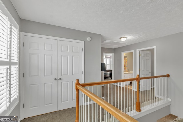 hall with an upstairs landing, a textured ceiling, attic access, and carpet