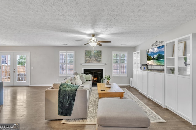 living area with a wealth of natural light, ceiling fan, a lit fireplace, and dark wood-style flooring