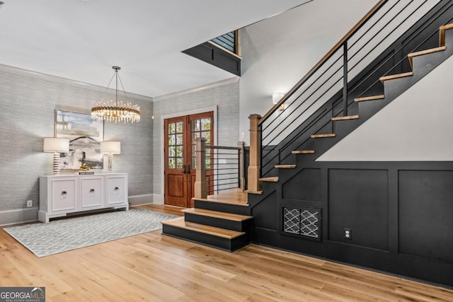 entryway with light wood-style flooring, a decorative wall, ornamental molding, french doors, and stairway