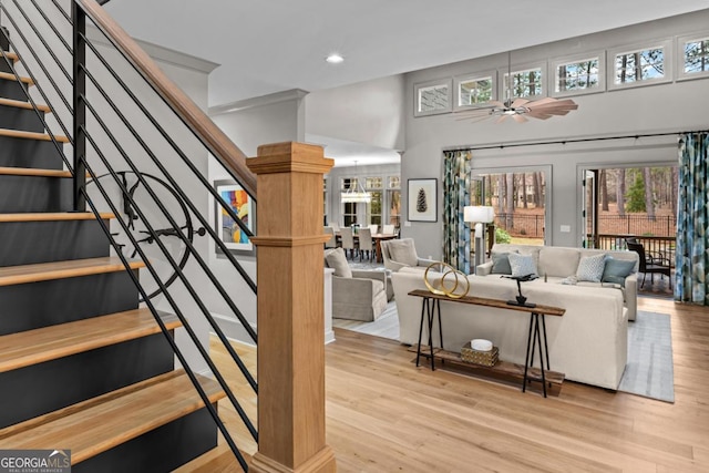 living area with a ceiling fan, wood finished floors, a towering ceiling, and stairs