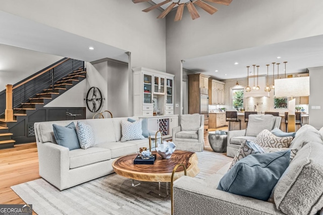 living area with recessed lighting, a high ceiling, a ceiling fan, light wood-type flooring, and stairs