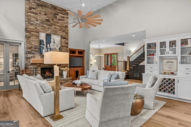 living room featuring french doors, a fireplace, a towering ceiling, light wood-type flooring, and stairs