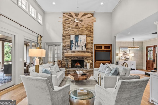 living room featuring a stone fireplace, a high ceiling, light wood-style floors, ornamental molding, and french doors