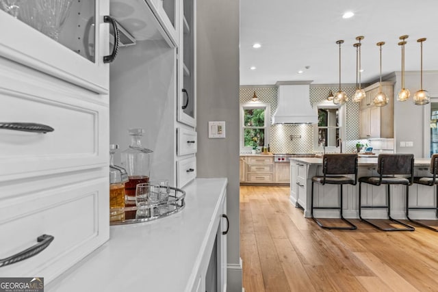 kitchen with light wood-style floors, hanging light fixtures, backsplash, a kitchen bar, and custom range hood