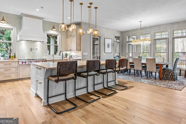 kitchen featuring an island with sink, stainless steel gas cooktop, custom exhaust hood, and light wood finished floors