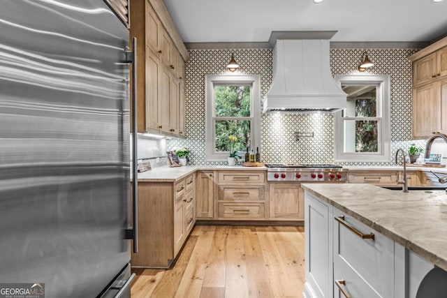 kitchen with custom range hood, appliances with stainless steel finishes, light wood-style floors, a sink, and wallpapered walls