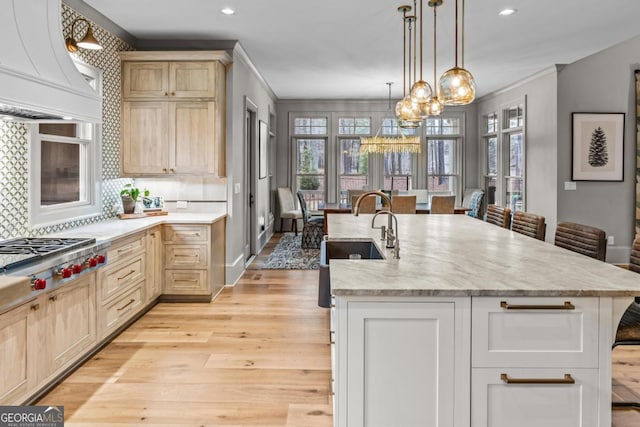 kitchen featuring a kitchen island with sink, a sink, light wood-style floors, custom exhaust hood, and stainless steel gas stovetop