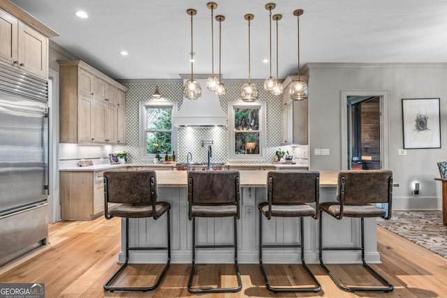 kitchen with built in fridge, light wood-type flooring, light countertops, and hanging light fixtures