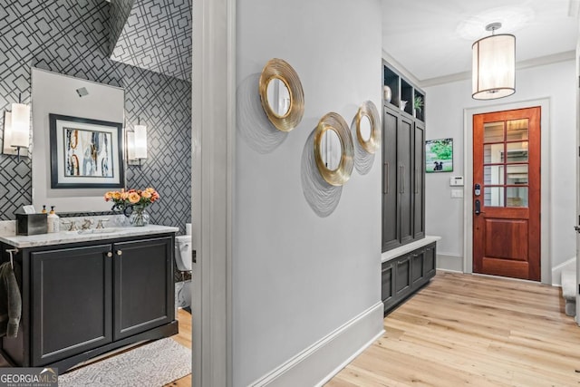 interior space with wallpapered walls, an accent wall, baseboards, and light wood finished floors