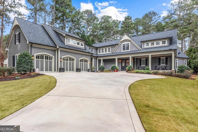 shingle-style home featuring covered porch, a shingled roof, a front lawn, and concrete driveway