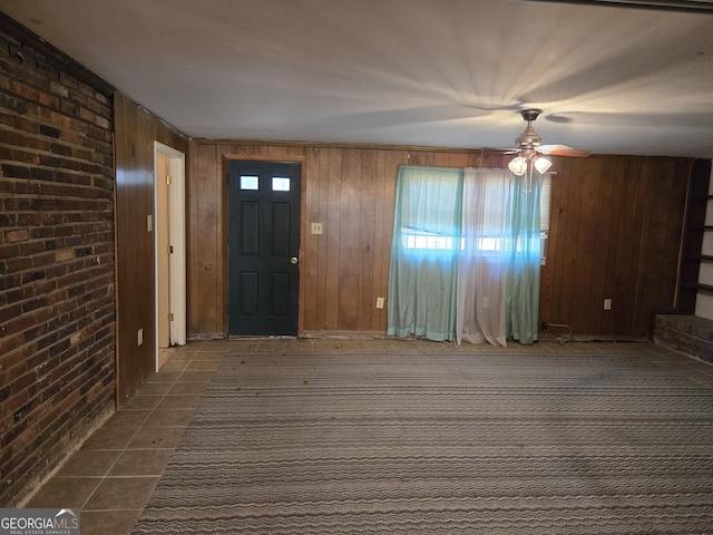 foyer featuring brick wall, dark tile patterned floors, a ceiling fan, and wooden walls