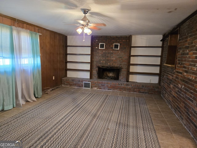 unfurnished living room featuring tile patterned flooring, brick wall, wood walls, visible vents, and a brick fireplace