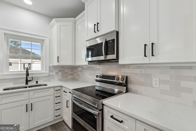 kitchen featuring a sink, tasteful backsplash, white cabinetry, appliances with stainless steel finishes, and light stone countertops