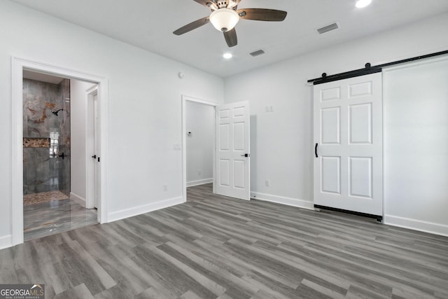 unfurnished bedroom with visible vents, a barn door, baseboards, and wood finished floors